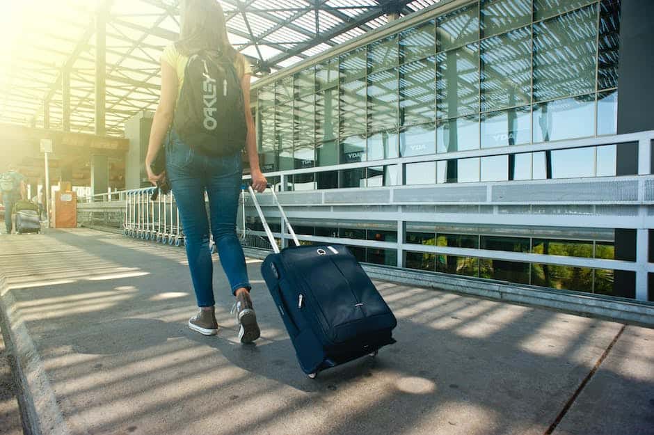 A woman with a backpack pulling a suitcase through an airport.