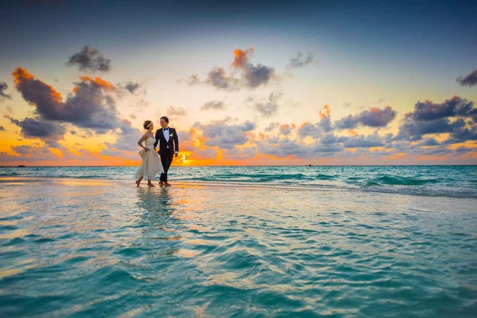 A bride and groom standing in the water at sunset.