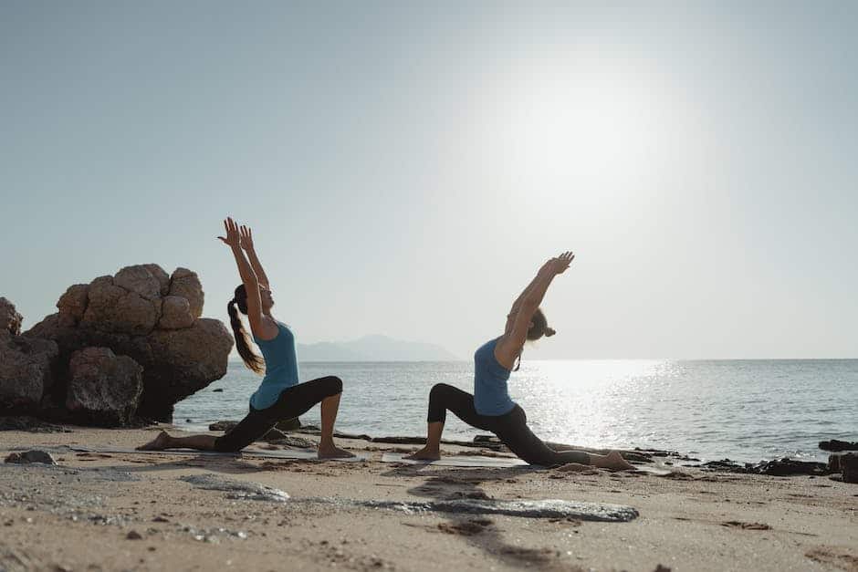 Two women doing yoga on the beach with the sun behind them.