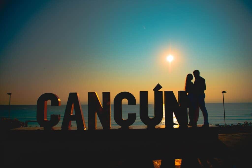 A couple standing in front of a sign that says Cancun, showcasing the best resorts for couples.