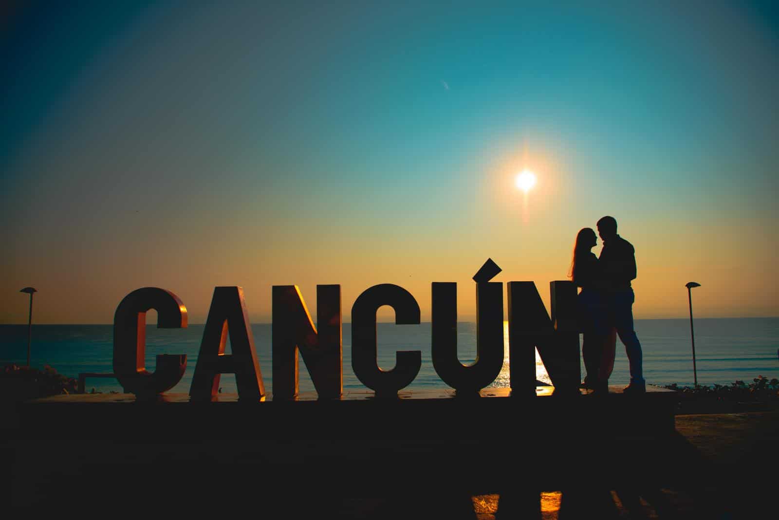 A couple standing in front of a sign that says Cancun, showcasing the best resorts for couples.