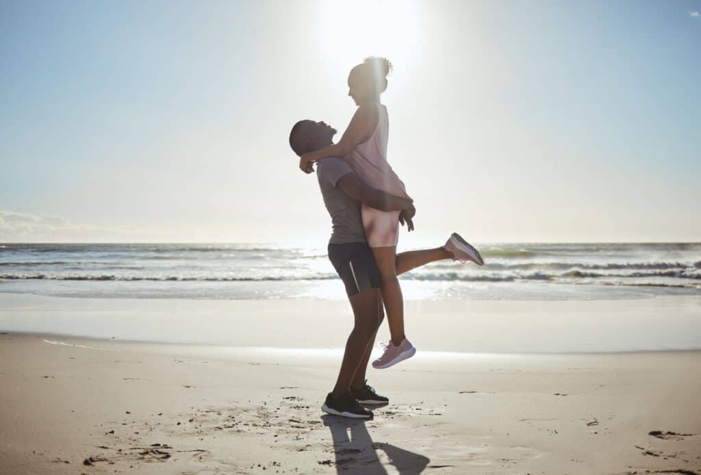 A man is carrying a woman on the sunny beach in Cancun during June.