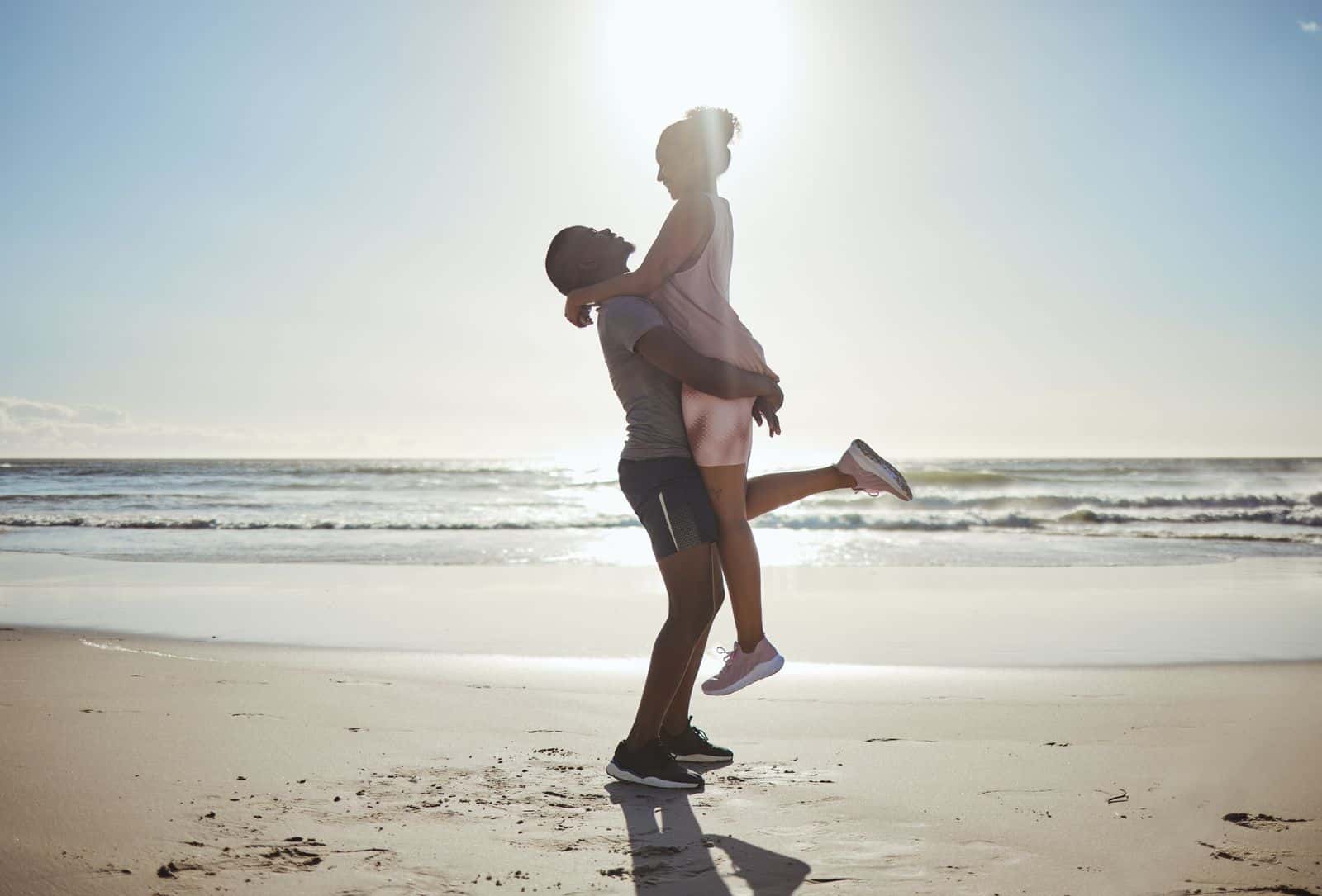 A man is carrying a woman on the sunny beach in Cancun during June.