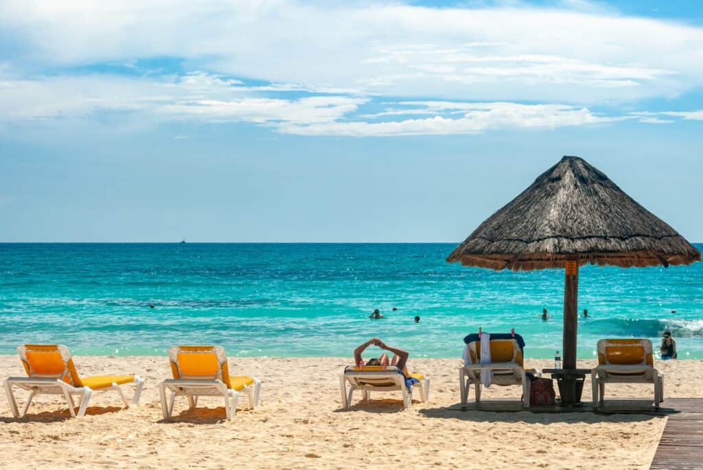 A beach with lounge chairs and a thatched umbrella at one of the best resorts with private beaches in Cancun.