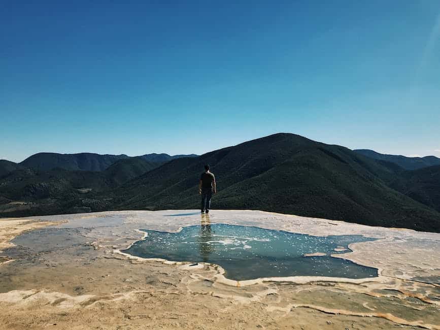 A man standing on top of a mountain looking at the water.