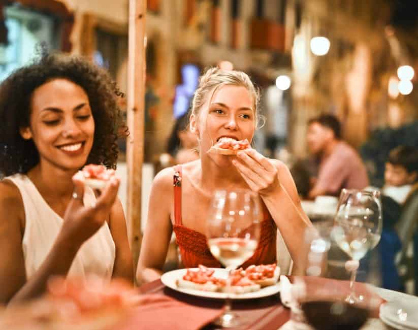 Two women eating pizza at an outdoor restaurant.