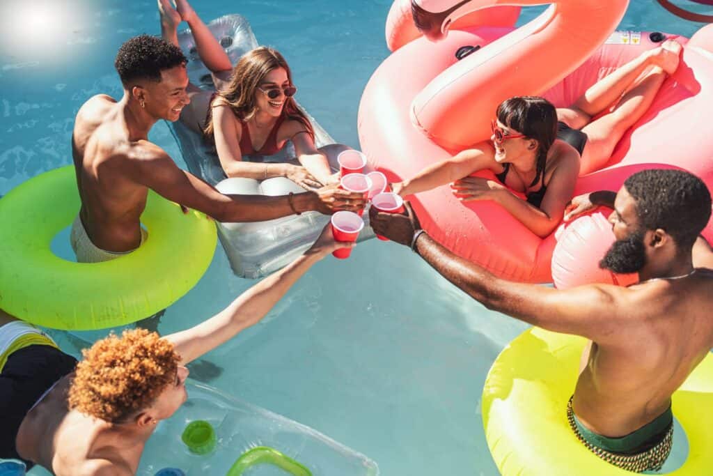 A group of people toasting in a pool with inflatable flamingos.