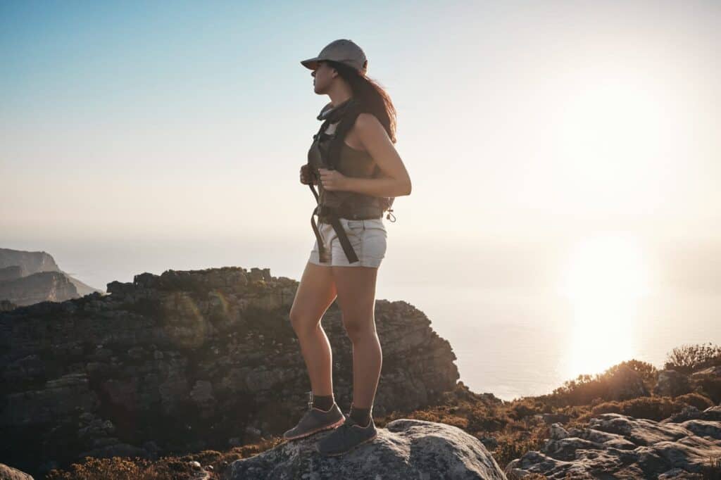 A woman is standing on top of a mountain overlooking the ocean.