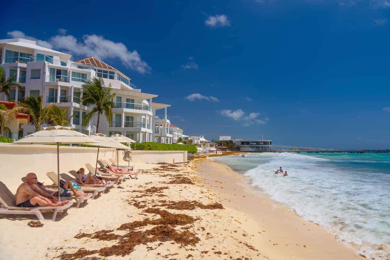 A beach with lounge chairs and umbrellas in front of a hotel.