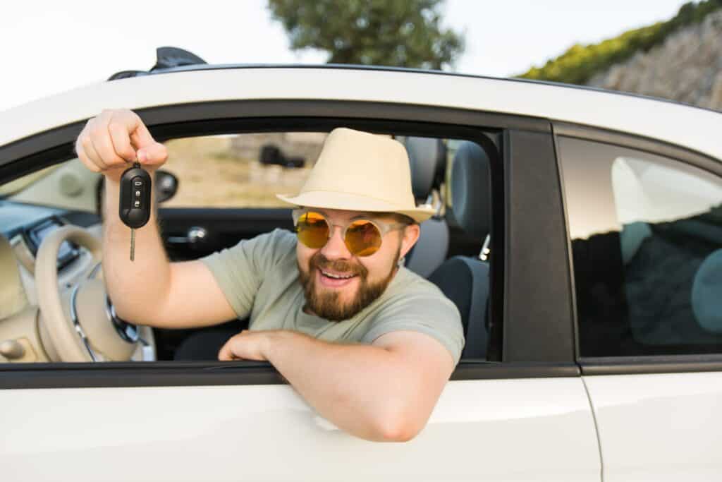 A man in a hat and sunglasses holding a car key.